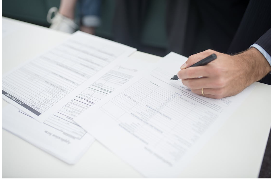 A hand holding a pen, filling out documents on a desk, symbolizing the paperwork required for a child’s passport